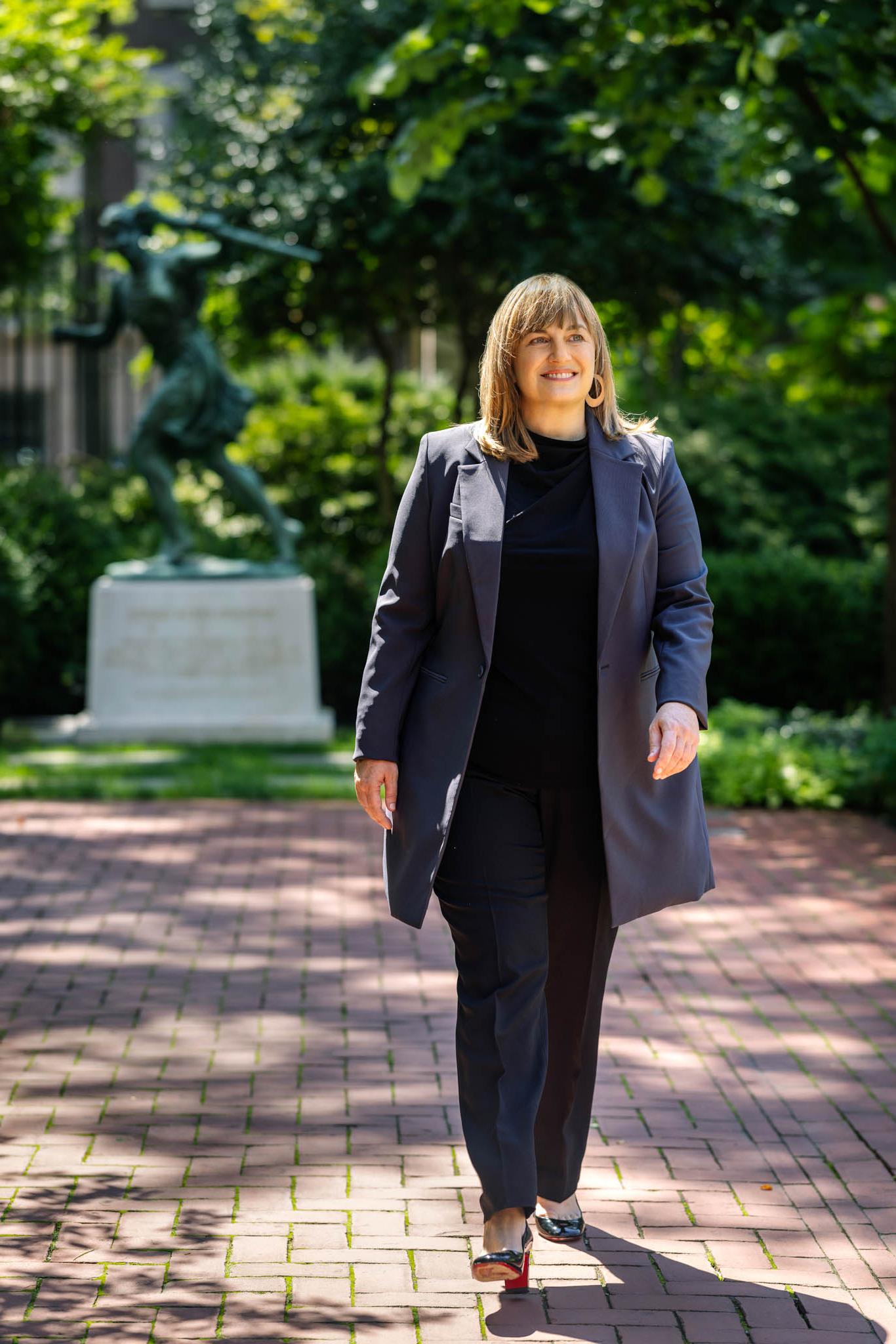 Laura Rosenbury walking on campus the athena statue is behind her